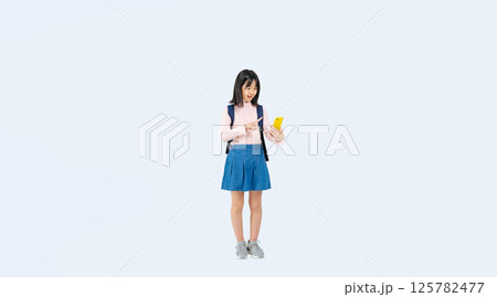 リュックを背負ってスマホを使う小学生の女の子の全身写真 リュックを背負ってスマホを使う小学生の女の子の全身写真 125782477