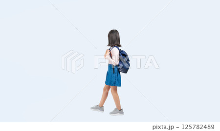 リュックを背負って横向きに歩く小学生の女の子の全身写真 125782489