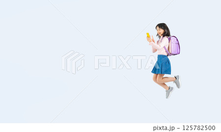 スマホを使いながらジャンプするランドセルを背負った小学生の女の子の全身写真 125782500