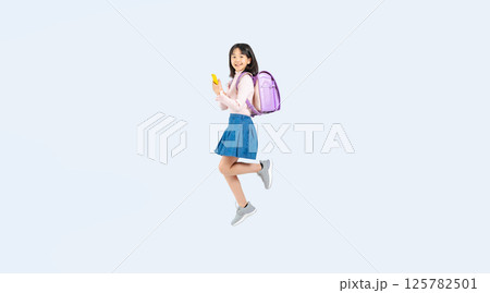 スマホを使いながらジャンプするランドセルを背負った小学生の女の子の全身写真 スマホを使いながらジャンプするランドセルを背負った小学生の女の子の全身写真 125782501