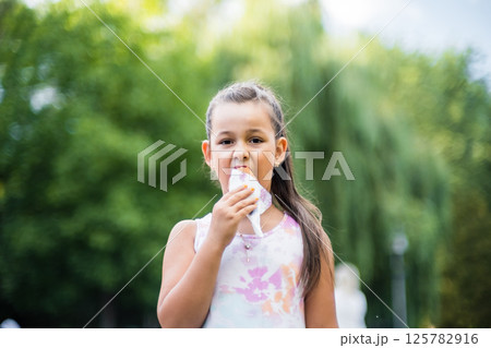 A cute child enjoys a delicious ice cream cone during the summer. Childs with ice cream on a walk in the city park. A cute child enjoys a delicious ice cream cone during the summer. Childs with ice cream on a walk in the city park. 125782916