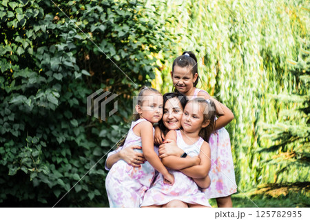 The girls stand side by side, arms wrapped around their mother. The twins laugh, pressing their cheeks against her. The girls stand side by side, arms wrapped around their mother. The twins laugh, pressing their cheeks against her. 125782935