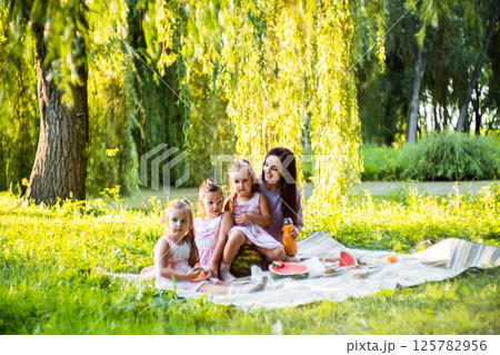 The picnic is full of joy as the girls enjoy their treat. The twins hold their slices carefully, giggling. 125782956
