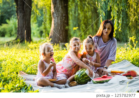 The sun shines as the family enjoys their picnic. The twins' hands are covered in watermelon juice. 125782977