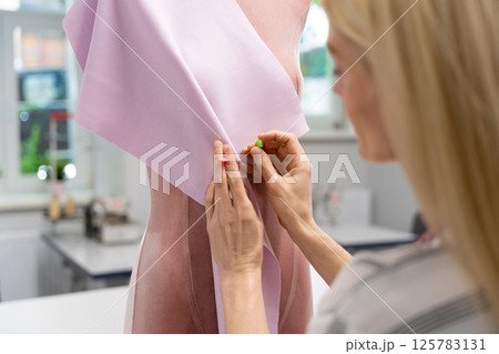 Blonde fashion designer standing near the dummy and trying a new model Blonde fashion designer standing near the dummy and trying a new model 125783131