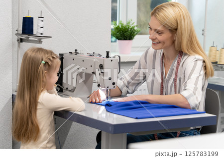 Blonde long-haired female dress designer in her studio with her daughter 125783199