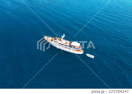 Aerial view of a luxurious yacht sailing on calm, deep blue ocean Aerial view of a luxurious yacht sailing on calm, deep blue ocean 125784247