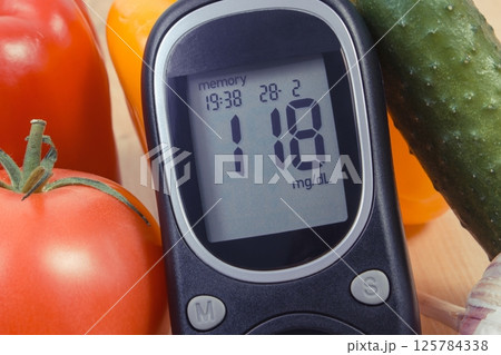 Glucose meter with result of sugar level and natural vegetables. Healthy nutrition during diabetes Glucose meter with result of sugar level and natural vegetables. Healthy nutrition during diabetes 125784338
