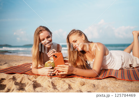 Friends Relaxing on the Beach, Drinking and Browsing on Their Smartphones 125784469