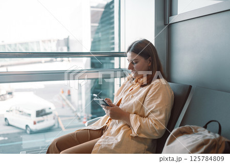 Young woman in the airport terminal using smartphones while waiting for her flight. Young woman in the airport terminal using smartphones while waiting for her flight. 125784809