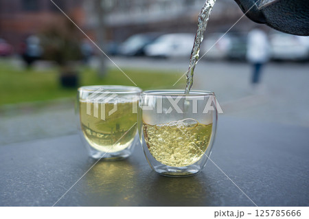 Pouring green tea into a glass from a metal kettle on blurred background, hot drink in teapot Pouring green tea into a glass from a metal kettle on blurred background, hot drink in teapot 125785666