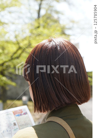 観光パンフレットを見る若い女性（タテ） 125785904