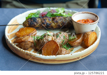 Georgian lula kebab plate. Bbq skewer, traditional barbecue dish with baked potatoes, sauce Georgian lula kebab plate. Bbq skewer, traditional barbecue dish with baked potatoes, sauce 125786221
