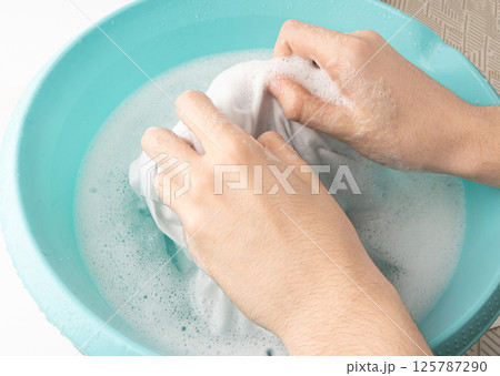 Hand laundry washing clothes in blue plastic basin 125787290