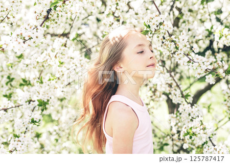 Young girl enjoying a peaceful childhood moment among blooming white cherry blossoms in a spring garden 125787417