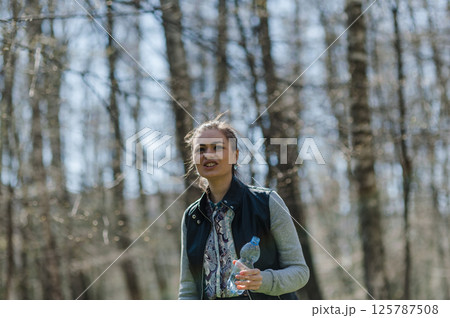 A young woman drinking water in the forest. A woman resting in a park and drinking mineral water from a plastic bottle A young woman drinking water in the forest. A woman resting in a park and drinking mineral water from a plastic bottle 125787508