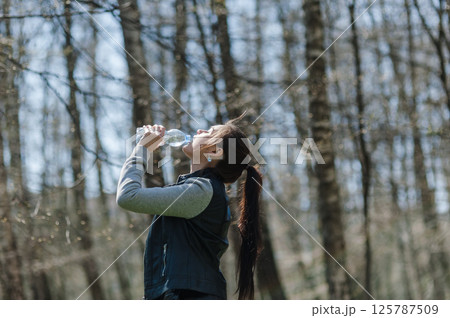 A young woman drinking water in the forest. A woman resting in a park and drinking mineral water from a plastic bottle. 125787509