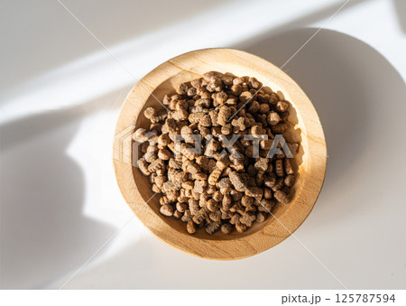 Dry pet food in sunlight, dog kibble pile, scattered puppy pellets, small canine protein croquette 125787594