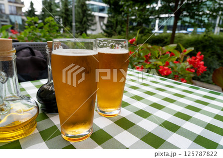 Two beer glasses at outdoor cafe, cold pint glass on checkered tablecloth table, cool condensation 125787822