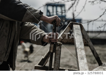 A pensioner repairs a trailer for a tractor. His hands shake from exhaustion.  125788031
