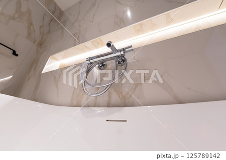 A modern chrome shower faucet on marble wall in a clean minimalist bathroom A modern chrome shower faucet on marble wall in a clean minimalist bathroom 125789142