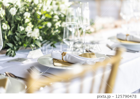 A wedding table covered with a white tablecloth, decorated with flowers, candles, glasses and cutlery 125790478