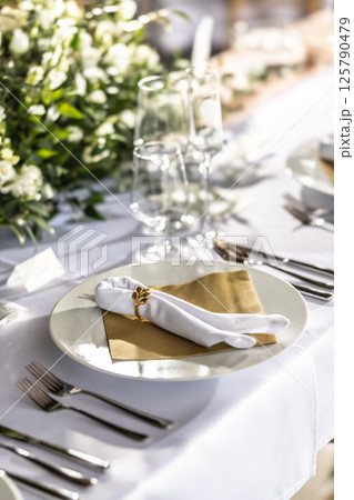 A wedding table covered with a white tablecloth, decorated with flowers, candles, glasses and cutlery A wedding table covered with a white tablecloth, decorated with flowers, candles, glasses and cutlery 125790479