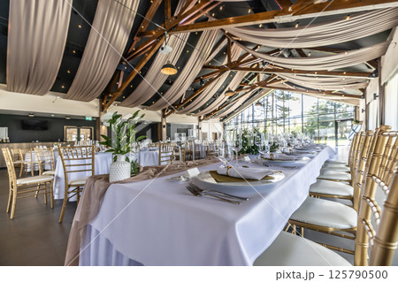 Wedding setting and decorated tables in a beautiful modern interior of a performance hall with a modern light ceiling of wooden construction 125790500