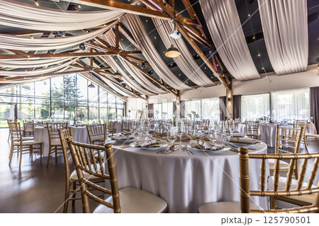 Wedding setting and decorated tables in a beautiful modern interior of a performance hall with a modern light ceiling of wooden construction 125790501