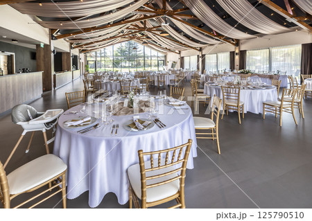 Wedding setting and decorated tables in a beautiful modern interior of a performance hall with a modern light ceiling of wooden construction 125790510