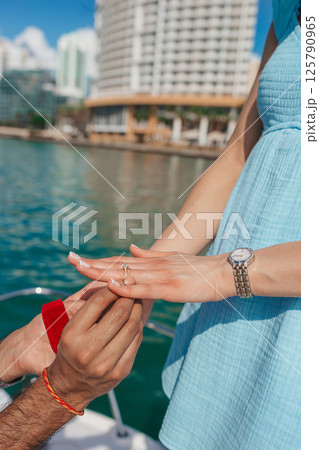 Closeup man putting engagement ring on woman hand on the boat 125790965