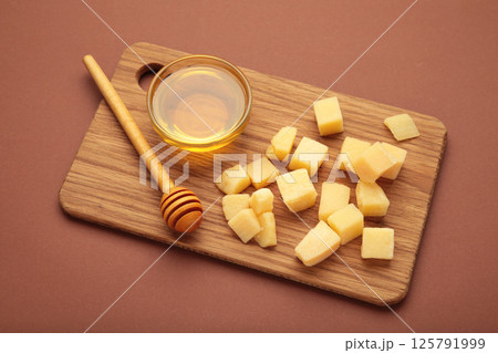 A piece of Parmesan cheese with honey on cutting board on brown background. 125791999