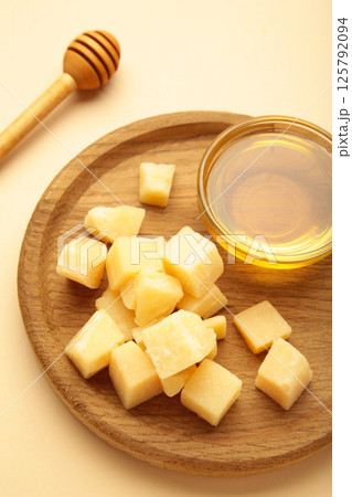 A piece of Parmesan cheese with honey on wooden plate on beige background. Vertical photo A piece of Parmesan cheese with honey on wooden plate on beige background. Vertical photo 125792094