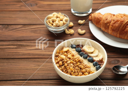 Beautiful morning breakfast with fresh croissants and granola with yoghurt on brown wooden background. Tasty and healthy breakfast Beautiful morning breakfast with fresh croissants and granola with yoghurt on brown wooden background. Tasty and healthy breakfast 125792225