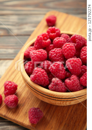 Raspberries in wooden bowl on brown background. Vertical photo 125792274