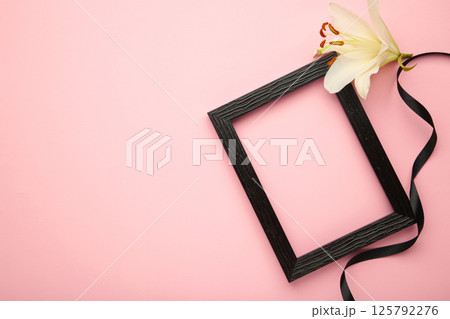 Beautiful lily flower with blank frame and black funeral ribbon on pink background 125792276