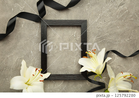 Beautiful lily flower with blank frame and black funeral ribbon on grey concrete background. Top view 125792280