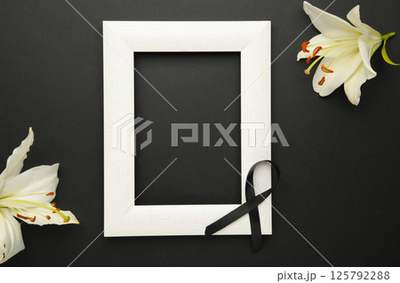 Beautiful lily flower with blank frame and black funeral ribbon on black background. Top view 125792288
