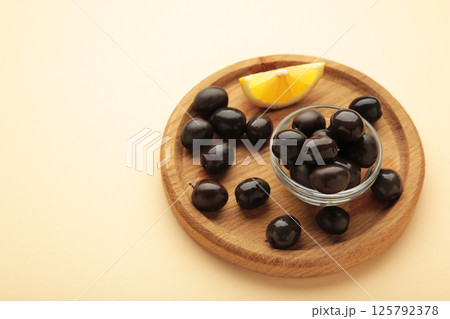 Black olives with lemon on wooden plate on beige background 125792378