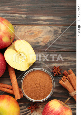 Red apple, cinnamon sticks and cinnamon in bowl on brown wooden background. Red apple, cinnamon sticks and cinnamon in bowl on brown wooden background. 125792621