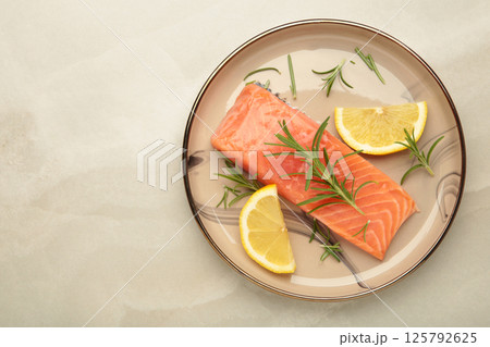 Red fish. Raw salmon fillet with rosemary and lemon on beige plate on grey background. Red fish. Raw salmon fillet with rosemary and lemon on beige plate on grey background. 125792625