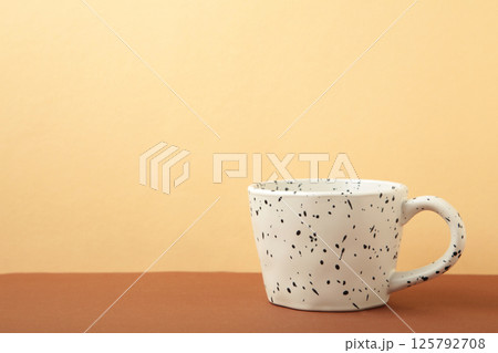 Ceramic white cup with black sparkles on beige background. Ceramic white cup with black sparkles on beige background. 125792708