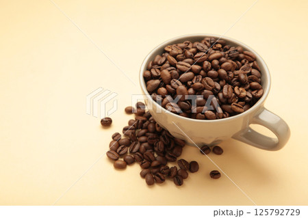 Coffee beans in coffee cup on beige background. Coffee beans in coffee cup on beige background. 125792729