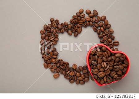 Coffee beans in the heart shaped bowl on grey background. Top view Coffee beans in the heart shaped bowl on grey background. Top view 125792817
