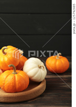 Autumn composition. Fresh orange and white pumpkin on wooden plate with autumn leaves on dark background. Top view 125792885