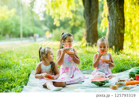 Three girls are holding pieces of watermelon in their hands. The beautiful girls are taking small bites of watermelon at a picnic. Three girls are holding pieces of watermelon in their hands. The beautiful girls are taking small bites of watermelon at a picnic. 125793319