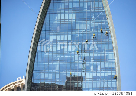Rope access workers suspended while cleaning the glass facade of a modern highrise office building 125794081