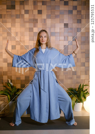 Yoga instructor in blue kimano at fitness gym . The girl does qigong yoga. The exercises are based on the movement of internal energy, the system of channels, energy centers, chakras Yoga instructor in blue kimano at fitness gym . The girl does qigong yoga. The exercises are based on the movement of internal energy, the system of channels, energy centers, chakras 125795531