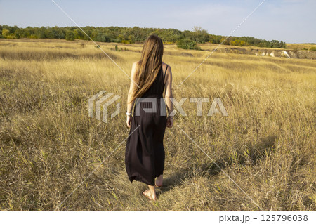Pretty young dark haired woman in black dress stand in field. Beautiful girl outdoor in the field enjoy with freedom 125796038