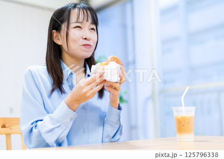 リビングで美味しそうにハンバーガーを食べる女性 リビングで美味しそうにハンバーガーを食べる女性 125796338
